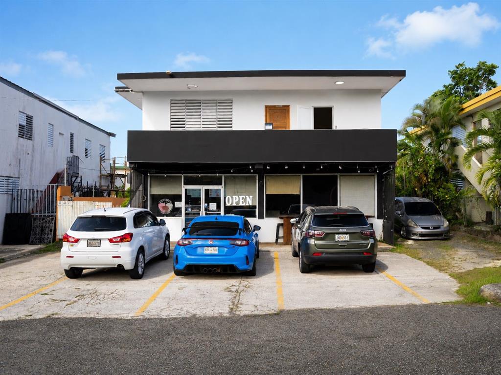 A two-story commercial building with three parked cars in front and an open sign — #2 St. CARR. JUAQUIN “YIYE” AVILA, QUEBRADILLAS, PR