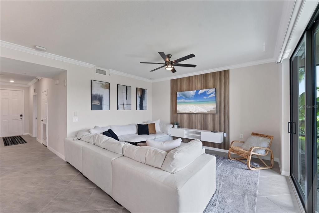 A living room features a white sectional sofa, a wall-mounted TV, and a wood-slatted accent wall — 17704 GAWTHROP DRIVE UNIT 102, BRADENTON, FL