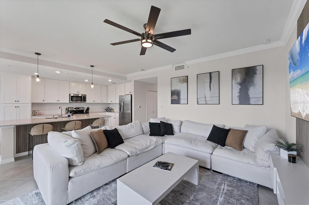 A modern living room with a large white sectional sofa, coffee table, and open kitchen — 17704 GAWTHROP DRIVE UNIT 102, BRADENTON, FL