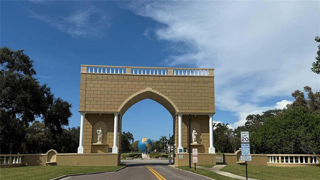 A large tan stone archway stands as an entrance to a property with a globe sculpture — 2460 CANADIAN WAY UNIT 48, CLEARWATER, FL