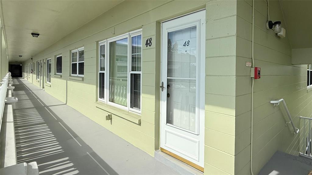 An exterior view of an apartment building walkway with light green walls and unit 48 — 2460 CANADIAN WAY UNIT 48, CLEARWATER, FL