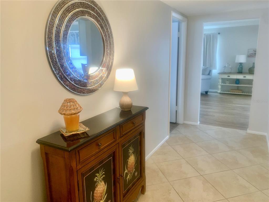 A wooden cabinet with pineapple motifs sits in a tiled entryway below a round mirror — 2310 CANALBLUFF PLACE UNIT V287, SARASOTA, FL