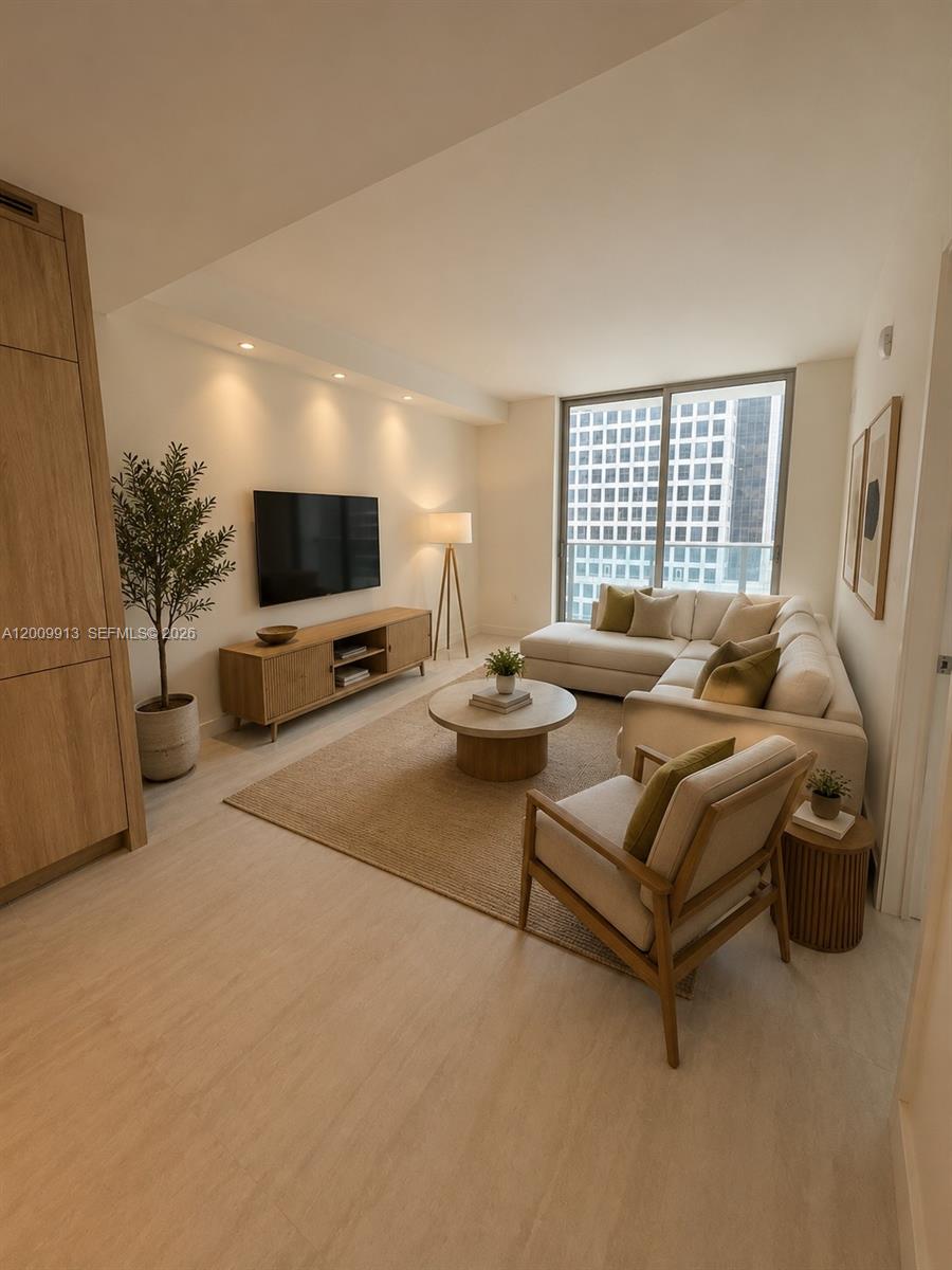 A modern living room features a sectional sofa, wooden media console, and floor-to-ceiling windows — 77 SE 5TH ST # 1811, Miami FL 33131, MIAMI, FL