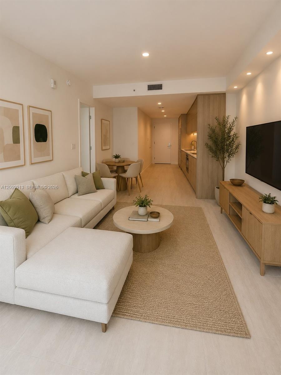 This open-concept living area features a white sectional sofa, a round coffee table, and a kitchen — 77 SE 5TH ST # 1811, Miami FL 33131, MIAMI, FL