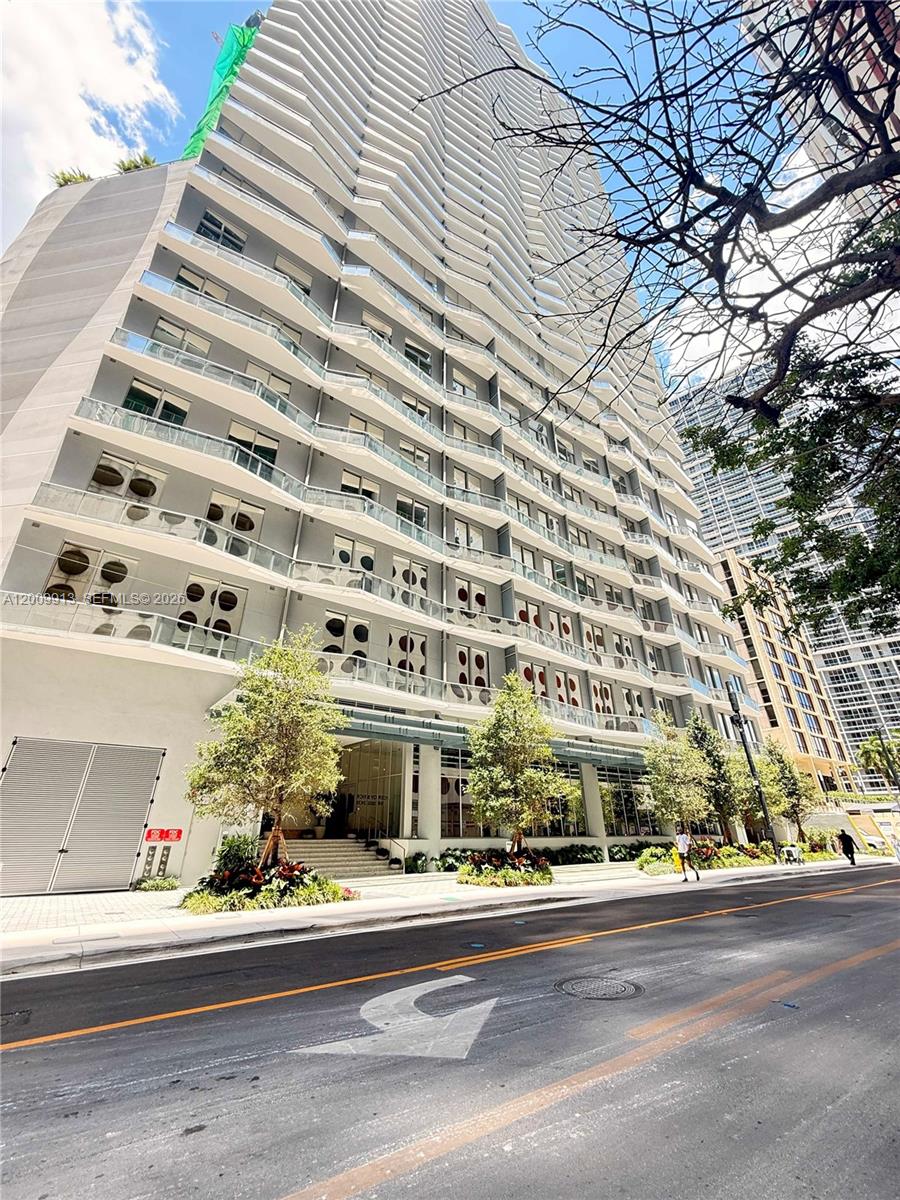 A low-angle exterior view of a modern high-rise apartment building with glass balconies — 77 SE 5TH ST # 1811, Miami FL 33131, MIAMI, FL