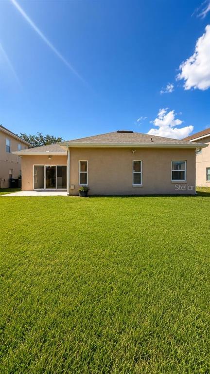 The rear exterior of a tan stucco house features a sliding glass door and windows — 1448 DERBY GLEN DRIVE, ORLANDO, FL