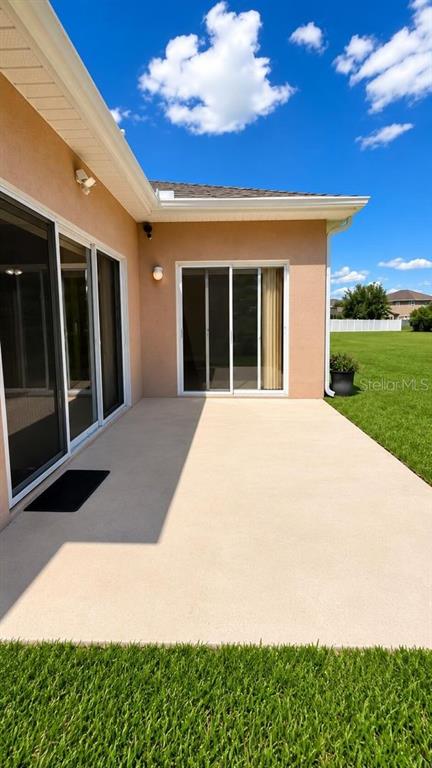 A concrete patio sits outside a house with sliding glass doors and a grassy yard — 1448 DERBY GLEN DRIVE, ORLANDO, FL