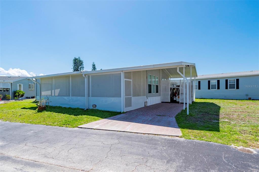 A light blue manufactured home features a screened-in porch and a paved carport — 1000 KINGS HIGHWAY UNIT 247, PORT CHARLOTTE, FL