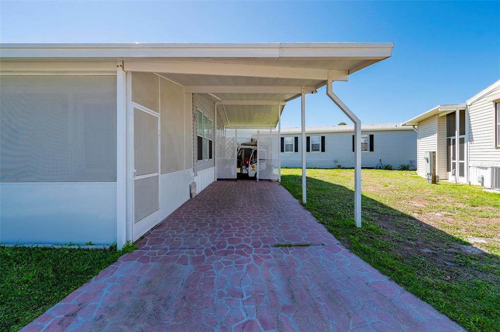 A covered carport with a patterned concrete floor sits beside a mobile home — 1000 KINGS HIGHWAY UNIT 247, PORT CHARLOTTE, FL