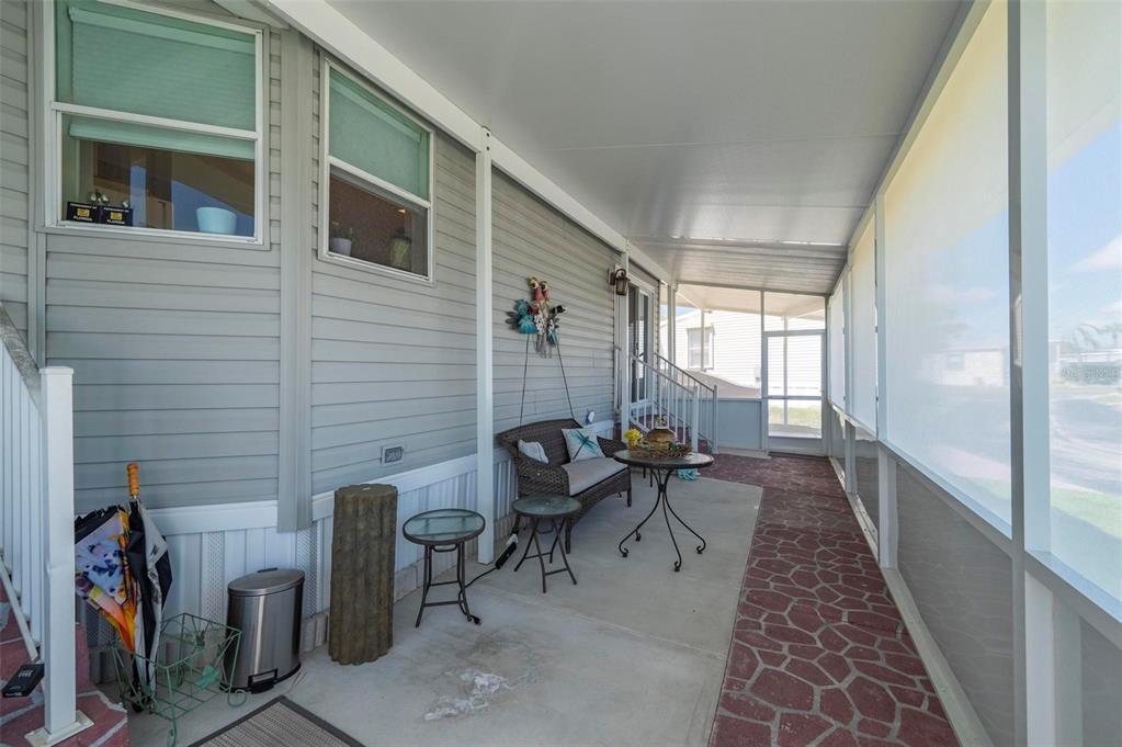 A covered patio features a concrete floor, a small seating area, and screen walls — 1000 KINGS HIGHWAY UNIT 247, PORT CHARLOTTE, FL