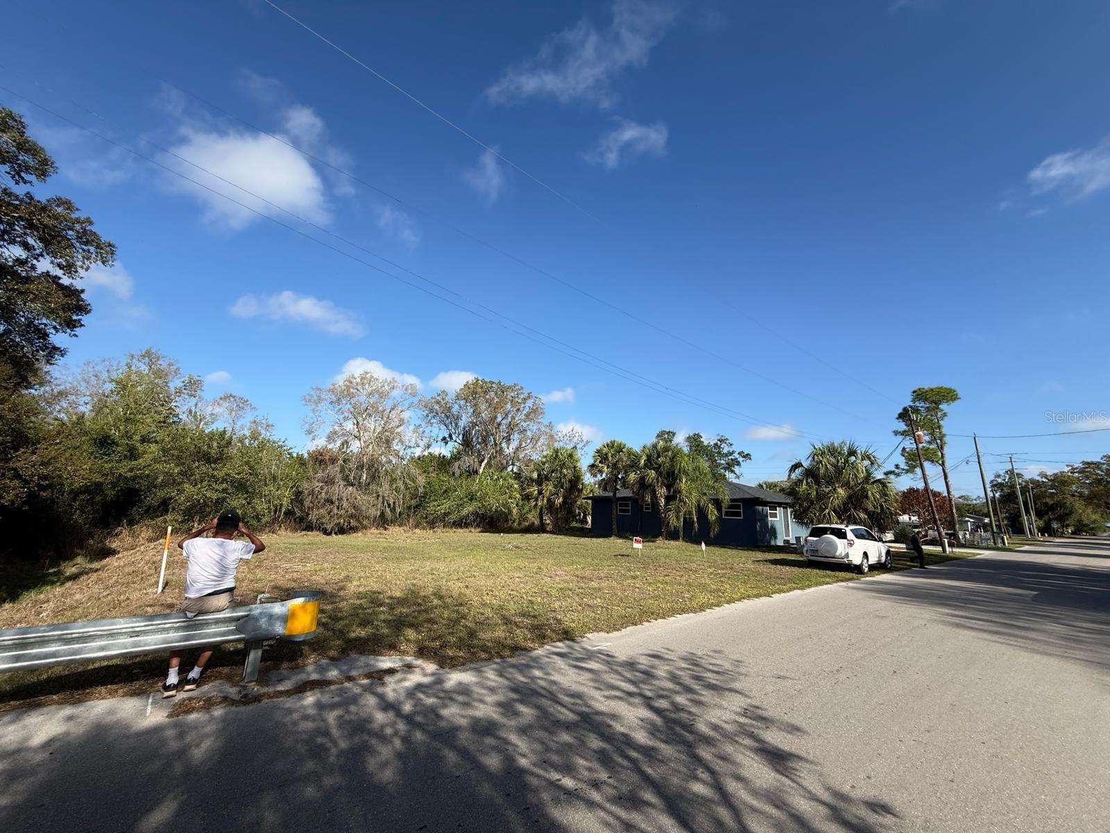 A person sits on a guardrail next to a vacant grassy lot and a house — Xxxx Singleton Avenue, FL 34266, FL