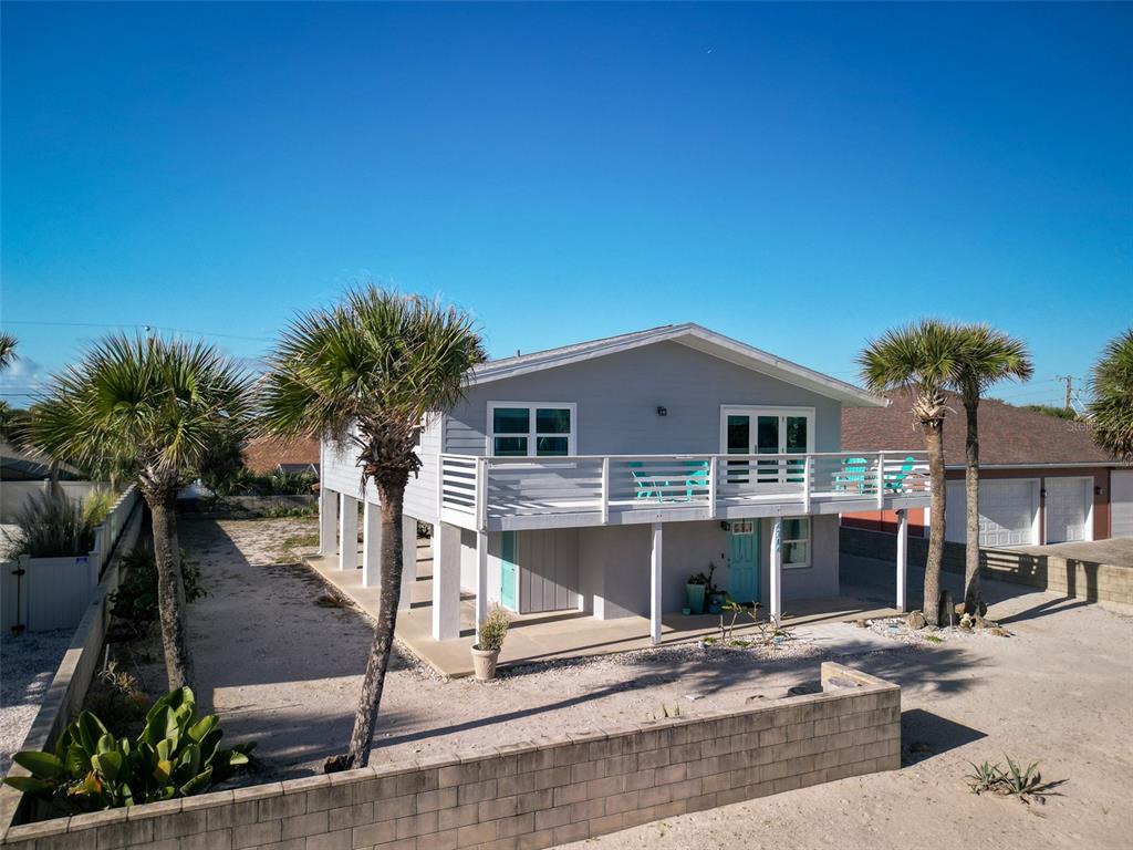 An elevated house with a deck, palm trees, and a concrete block wall in front — 4704 VAN KLEECK DRIVE, NEW SMYRNA BEACH, FL
