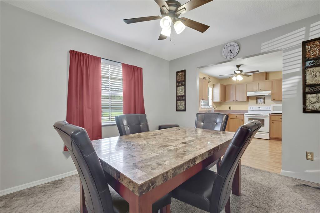 A dining room with a stone-topped table and dark chairs sits before an open kitchen — 7499 WABASH TRAIL, SPRING HILL, FL