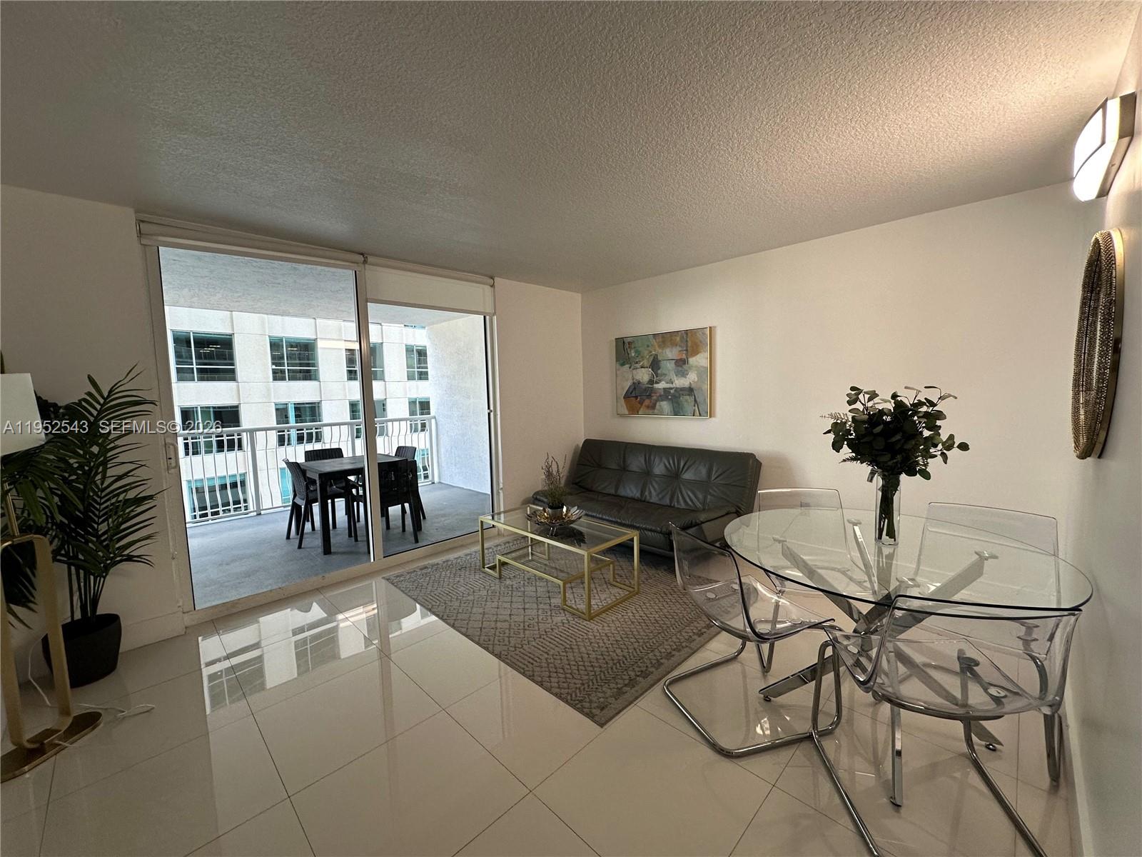 A living and dining area features white tile floors, a glass table, and a balcony — 1200 Brickell Bay Dr # 1712, Miami FL 33131, MIAMI, FL