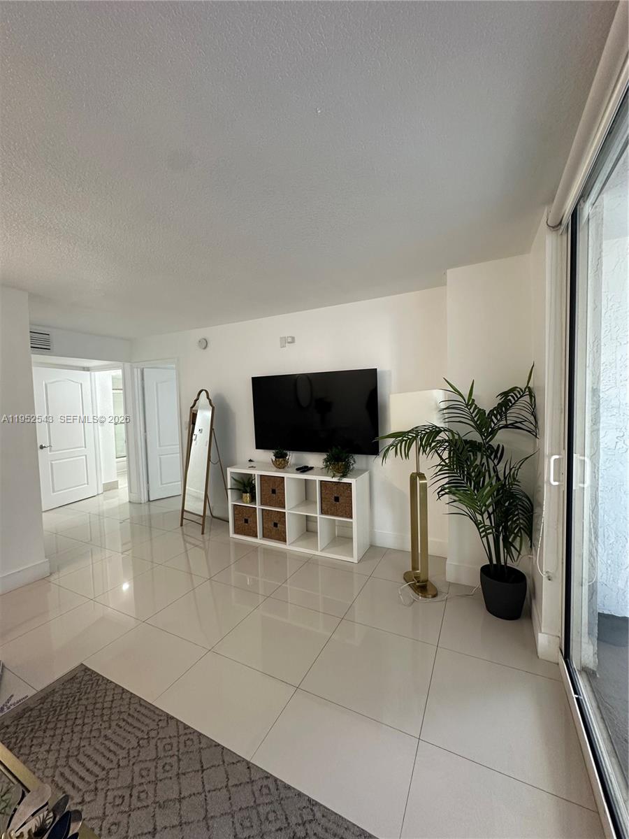 A living room features white tile floors, a wall-mounted television, and a white storage unit — 1200 Brickell Bay Dr # 1712, Miami FL 33131, MIAMI, FL