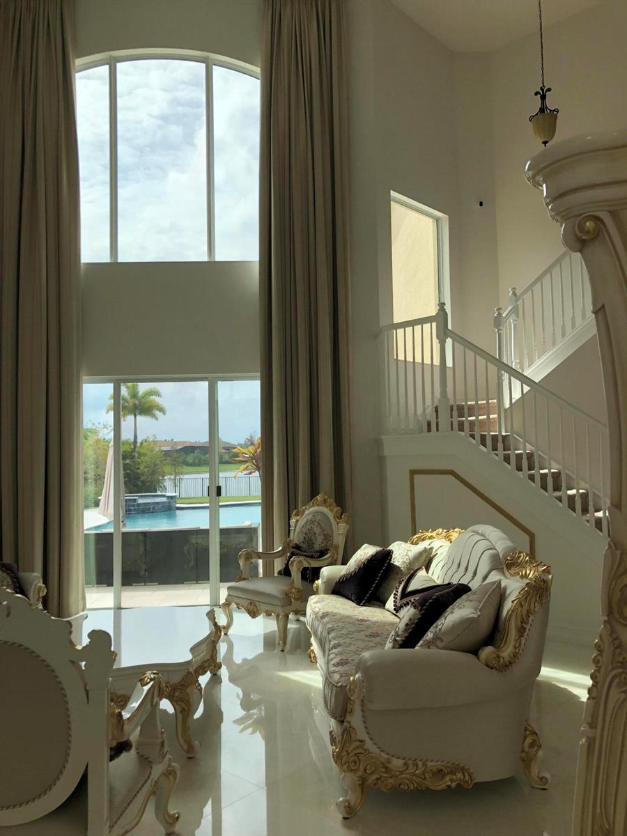 A high-ceilinged living room features ornate white furniture, a staircase, and a view of a pool — 7793 Arbor Crest Way, West Palm Beach FL 33412, WEST PALM BEACH, FL