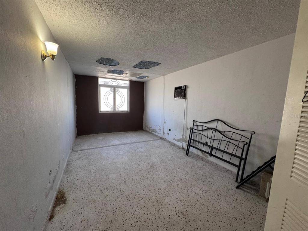 An empty bedroom features a metal bed frame, a window, and damaged ceiling and walls — 2S-2 URB METROPOLIS, CAROLINA, PR