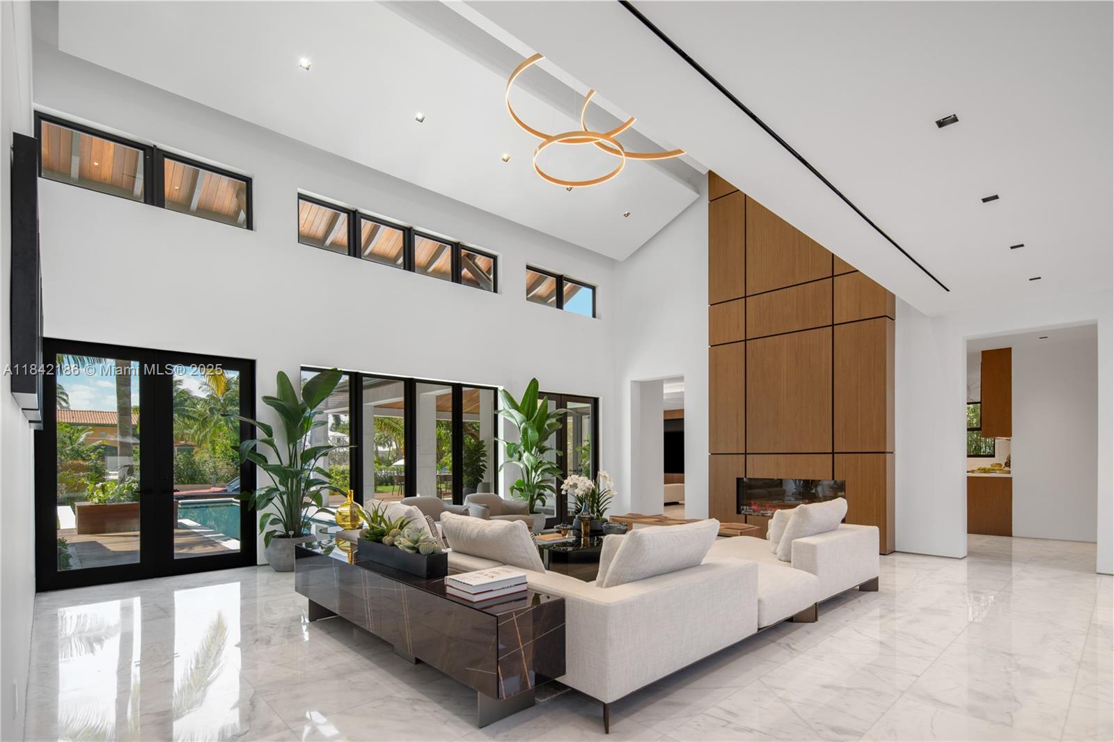 A modern living room features high ceilings, a large sectional sofa, and a wood-paneled fireplace — 4241 Palm Ln, Miami FL 33137, MIAMI, FL