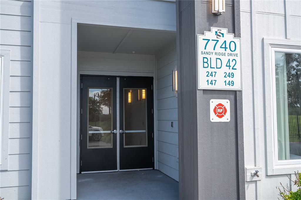 The exterior entrance of a multi-unit building features double glass doors and unit signage — 7740 SANDY RIDGE DRIVE UNIT 247, REUNION, FL