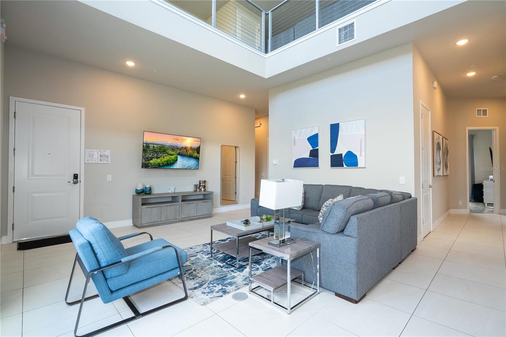 A living room features a high ceiling, tile flooring, a grey sectional, and a blue chair — 7740 SANDY RIDGE DRIVE UNIT 247, REUNION, FL