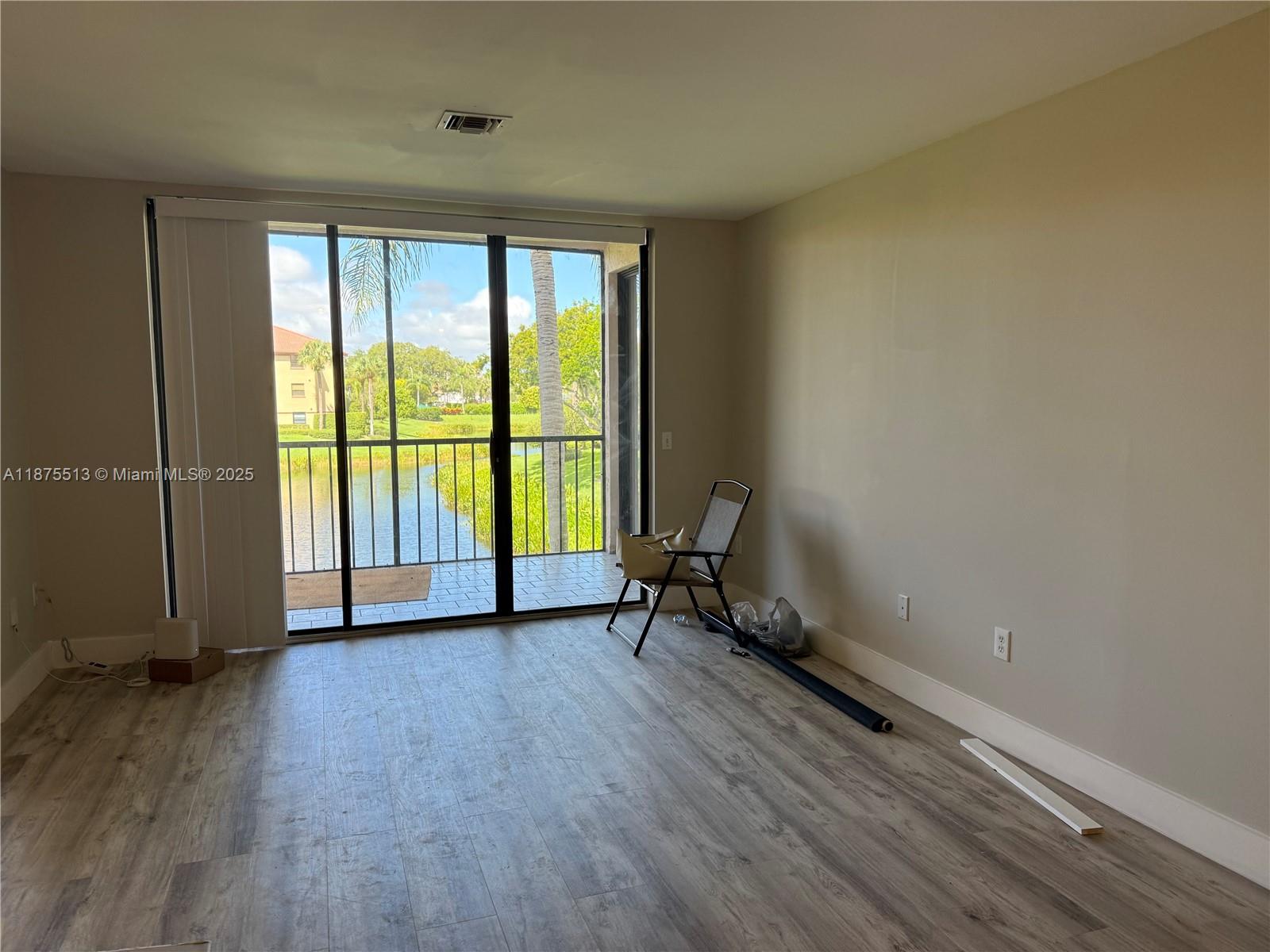 An empty room features light wood-look flooring, beige walls, and a sliding glass door to a balcony — 5147 Europa Dr, Boynton Beach FL 33437, BOYNTON BEACH, FL