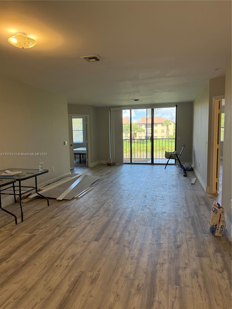 This living area features wood-look flooring, a sliding glass door, and an adjacent balcony view — 5147 Europa Dr, Boynton Beach FL 33437, BOYNTON BEACH, FL