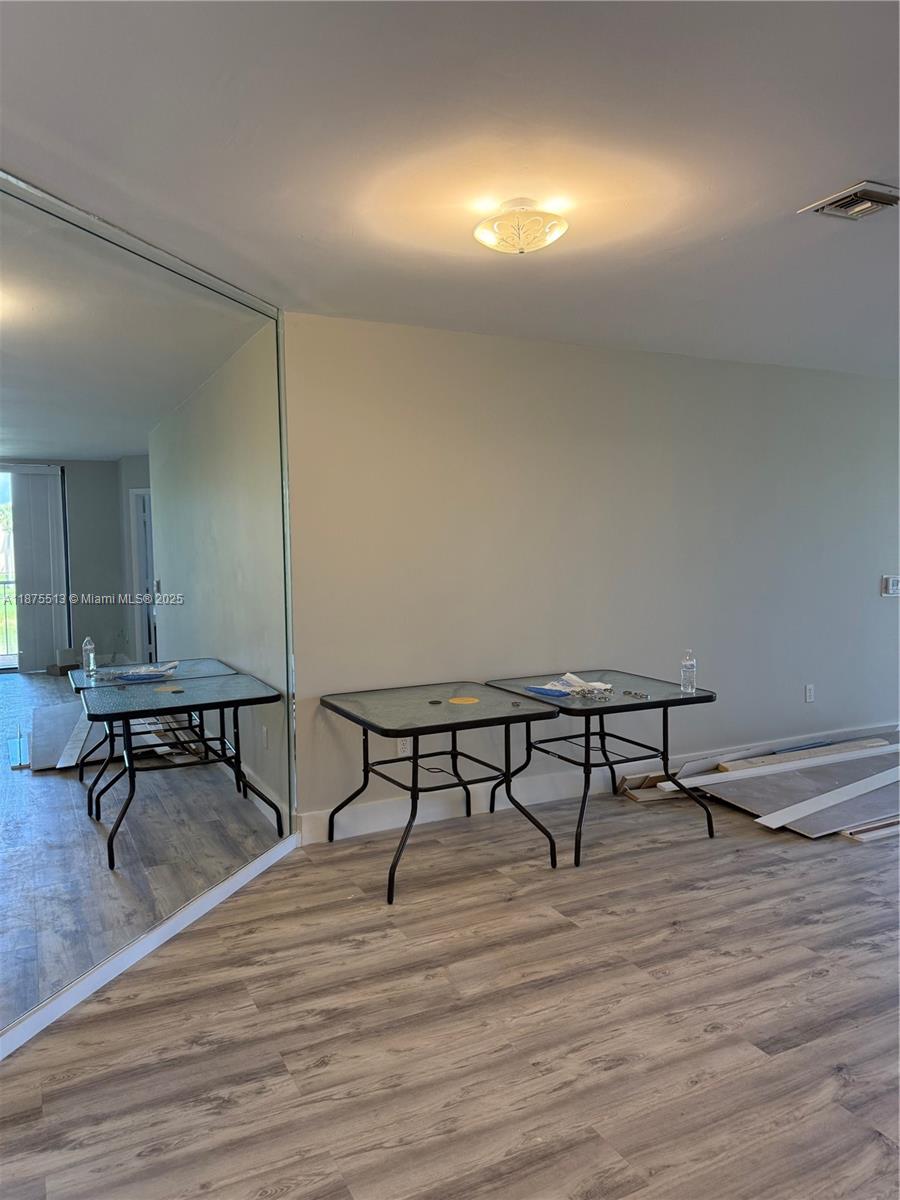 A room with wood-look flooring, a large wall mirror, and two small glass-top tables — 5147 Europa Dr, Boynton Beach FL 33437, BOYNTON BEACH, FL