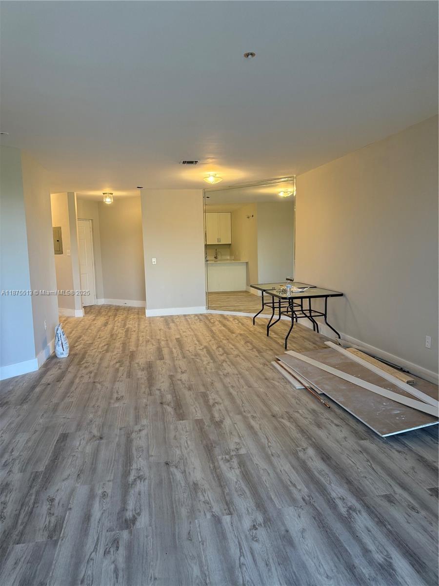 An empty room features light wood-look flooring, a mirrored wall, and a small dining table — 5147 Europa Dr, Boynton Beach FL 33437, BOYNTON BEACH, FL
