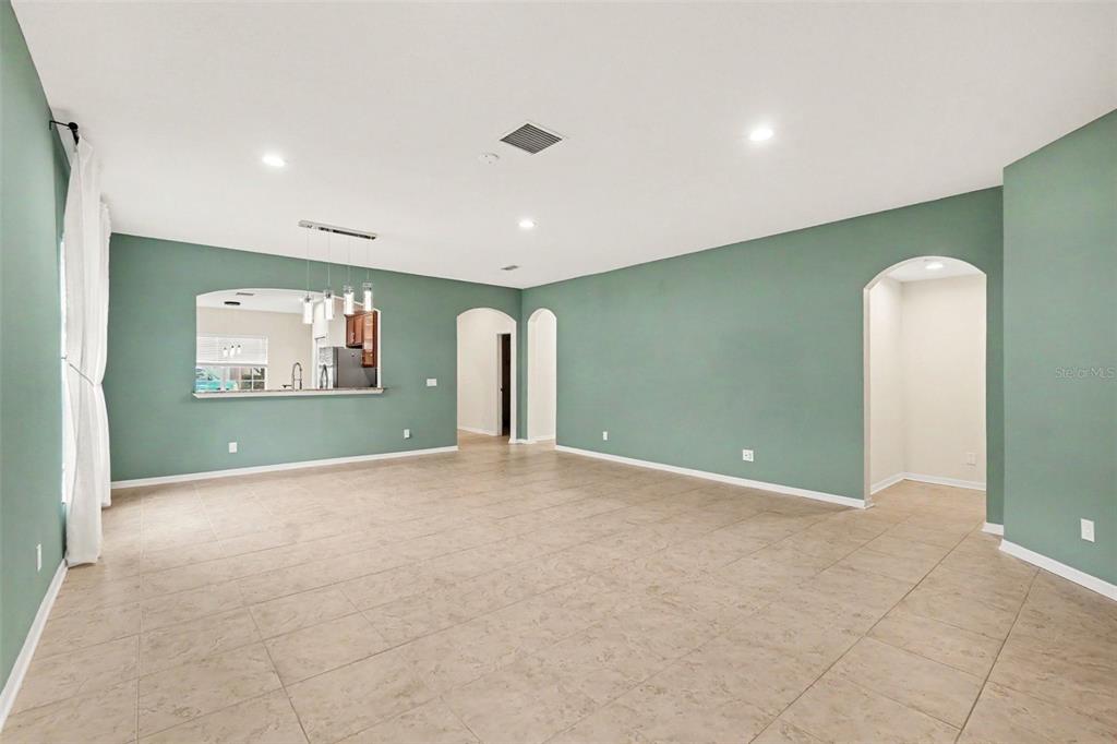 An empty living room features sage green walls, light tile flooring, and arched doorways — 7610 TANGLE BROOK BOULEVARD, GIBSONTON, FL