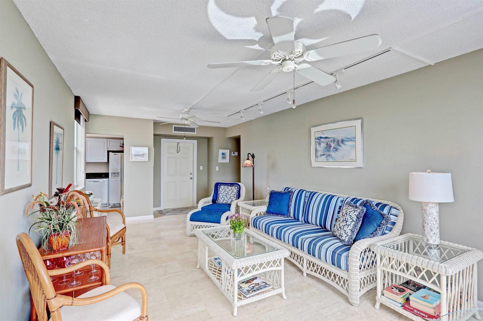 A living room features white wicker furniture, blue striped upholstery, and light tile flooring — 1820 New Palm Way # 201, Boynton Beach FL 33435, BOYNTON BEACH, FL