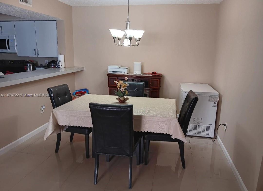 A dining area features a table with four chairs, a chandelier, and a wooden sideboard — 18870 NW 57th Ave # 108, Hialeah FL 33015, HIALEAH, FL
