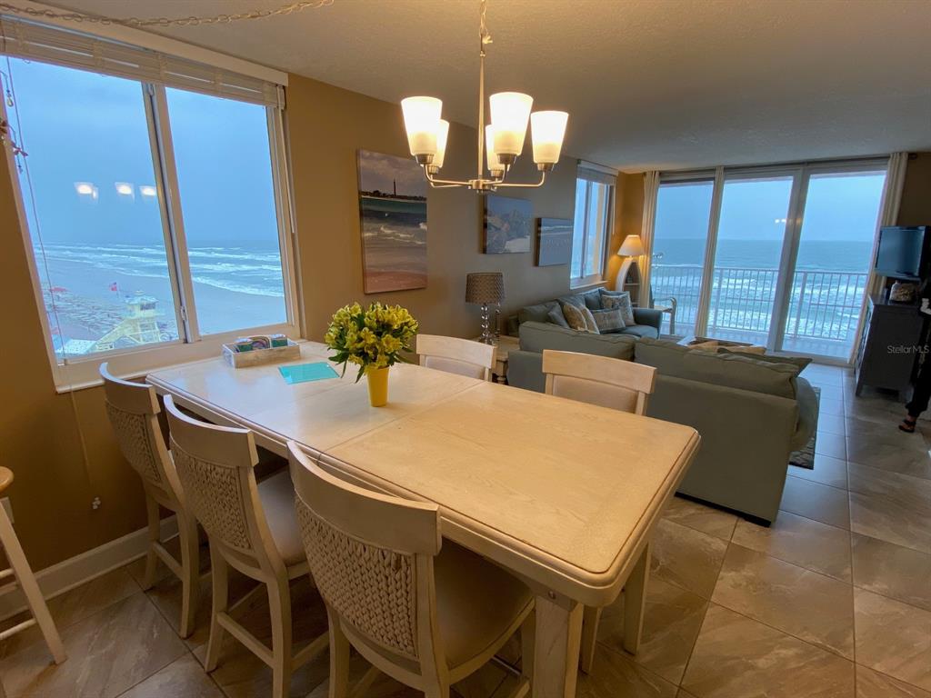 A dining area with a light wood table and chairs overlooks the ocean through windows — 421 SOUTH ATLANTIC AVENUE UNIT 806, NEW SMYRNA BEACH, FL