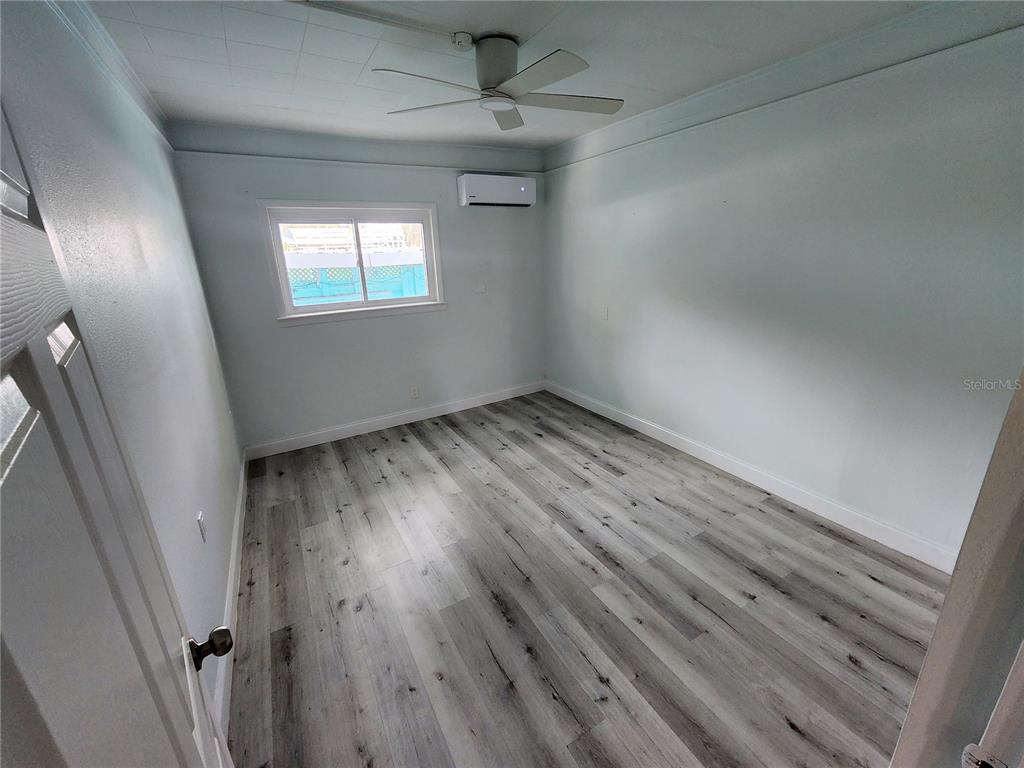 An empty bedroom features light gray walls, wood-look flooring, a ceiling fan, and a wall-mounted AC unit — 318 N DIXIE FREEWAY UNIT C, NEW SMYRNA BEACH, FL
