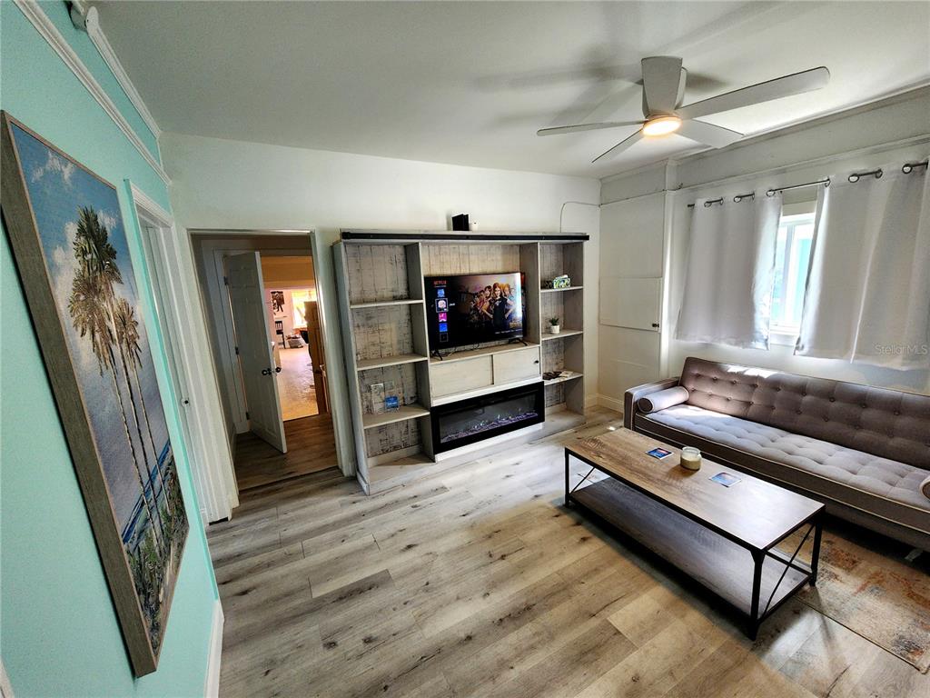 A living room features light wood-look flooring, a gray tufted sofa, and a built-in media unit — 318 N DIXIE FREEWAY UNIT C, NEW SMYRNA BEACH, FL
