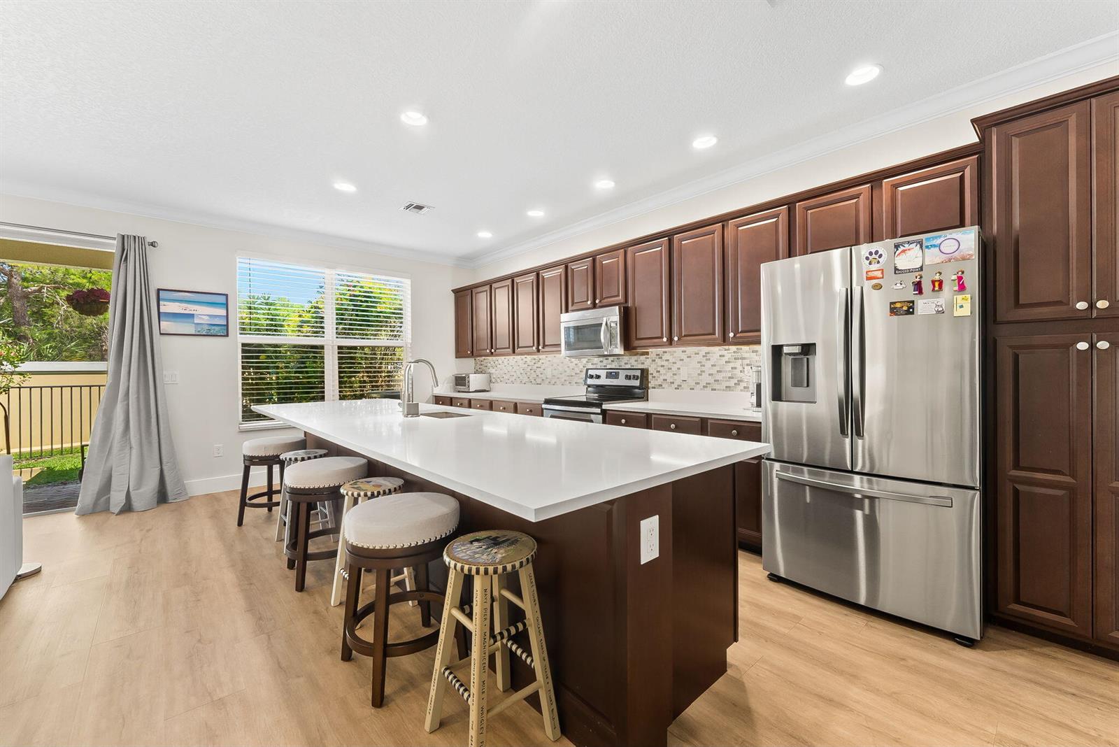 A kitchen features dark wood cabinets, a white quartz island with stools, and stainless appliances — 4865 NW 16th Terrace, Boca Raton FL 33431, BOCA RATON, FL