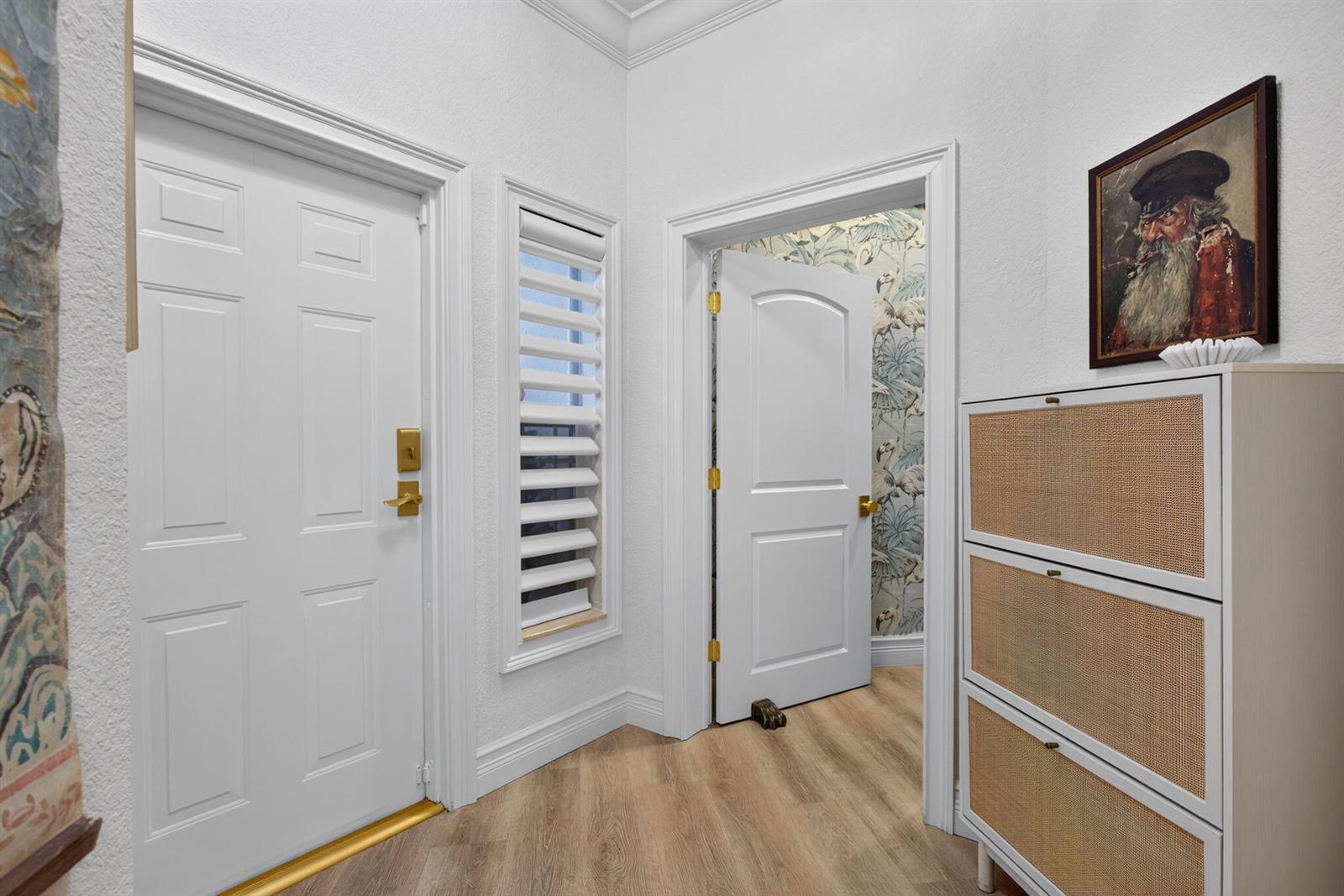 A white hallway features a door, a narrow window, a doorway with patterned wallpaper, and furniture — 2505 NE 2nd Street, Pompano Beach FL 33062, POMPANO BEACH, FL