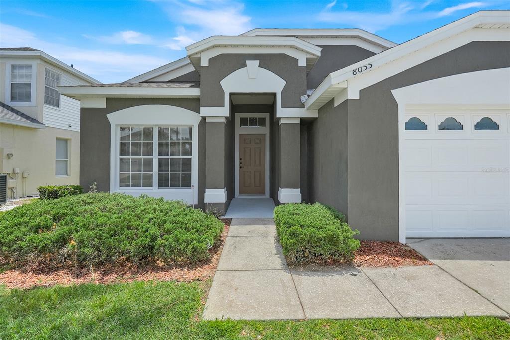 A single-story house with a gray stucco exterior, white trim, and a two-car garage — 8055 KING PALM CIRCLE, KISSIMMEE, FL