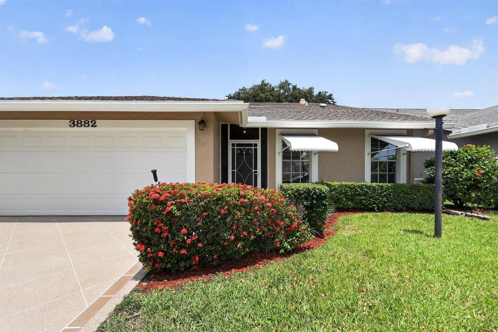 A single-story house exterior features a two-car garage, a front entrance, and landscaped flower beds — 3882 Dafilee Circle, West Palm Beach FL 33417, WEST PALM BEACH, FL