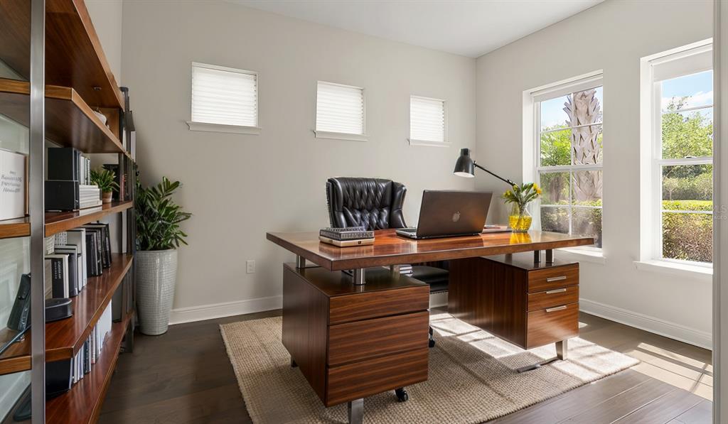 A home office features a wooden desk, leather chair, bookshelf, and windows with outdoor views — 8724 PEACHTREE PARK COURT, WINDERMERE, FL