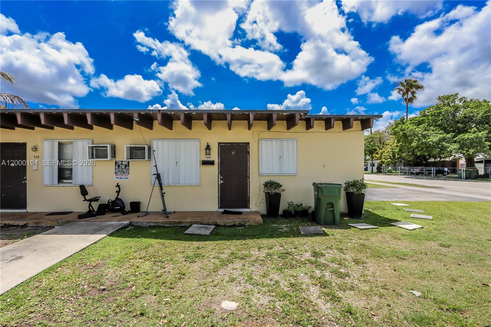 The exterior of a single-story yellow building features a brown door, window shutters, and exercise equipment — 720 SW 6th St, Homestead FL 33030, HOMESTEAD, FL