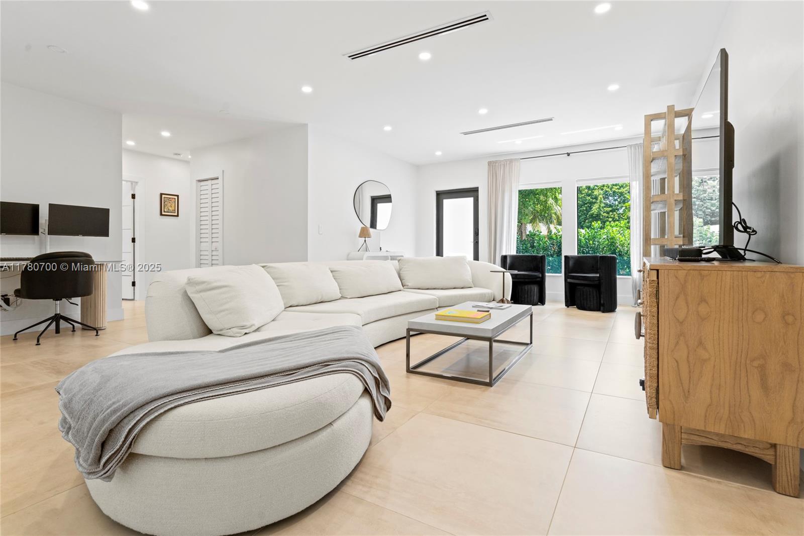 A bright living room features a large white sectional sofa, tile flooring, and a television — 281 NE 48th Ter, Miami FL 33137, MIAMI, FL