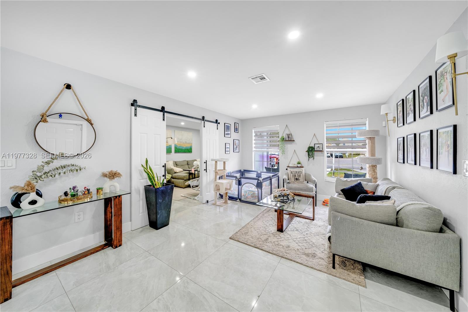 A living room features light tile floors, a grey sofa, and a sliding barn door — 14531 SW 127th Ct, Miami FL 33186, MIAMI, FL