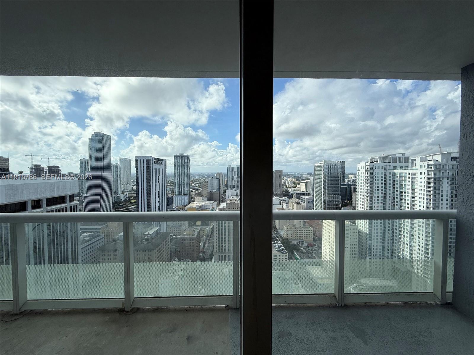 A balcony with a glass railing overlooks a dense city skyline under a cloudy sky — 50 Biscayne Blvd # 3911, Miami FL 33132, MIAMI, FL