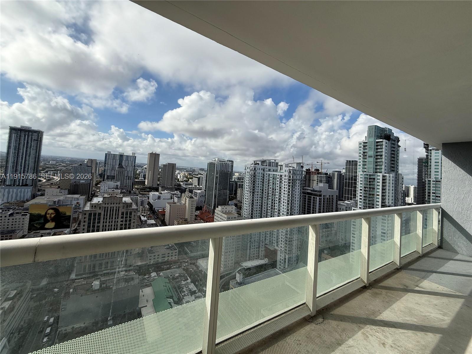 A high-rise balcony overlooks a dense city skyline under a partly cloudy sky — 50 Biscayne Blvd # 3911, Miami FL 33132, MIAMI, FL