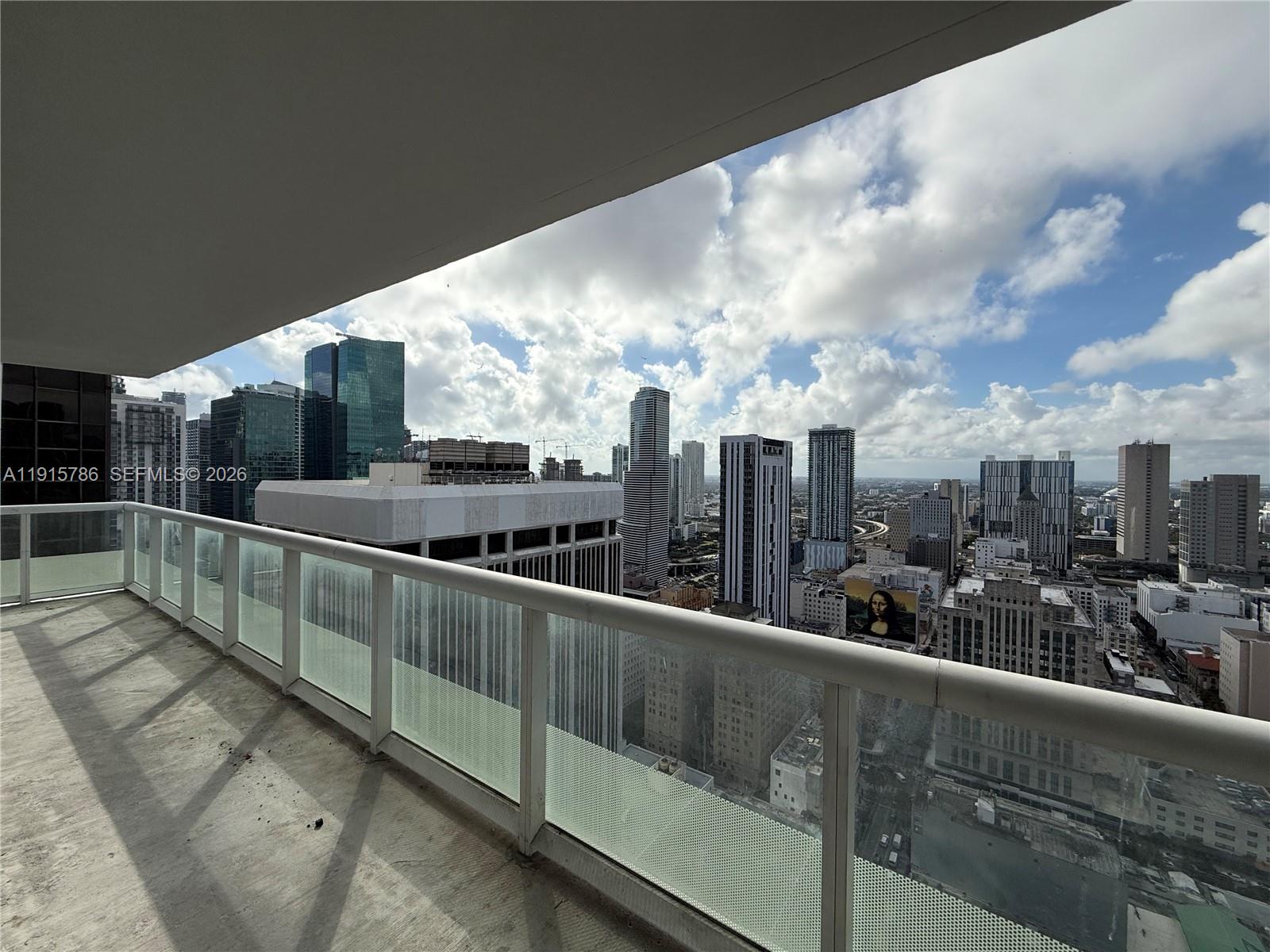 A high-rise balcony with a glass railing overlooks a dense urban skyline under a cloudy sky — 50 Biscayne Blvd # 3911, Miami FL 33132, MIAMI, FL