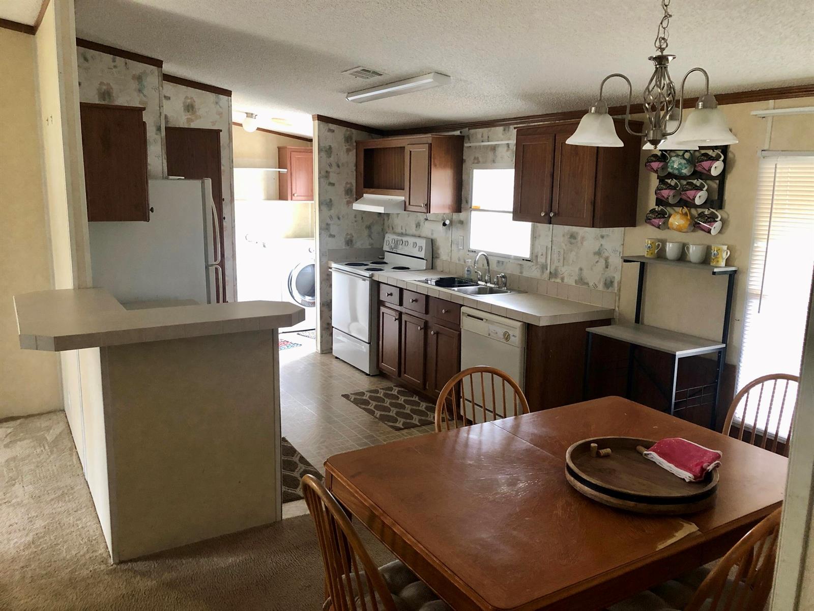 A kitchen with wood cabinets, white appliances, and a dining table in the foreground — 19720 NW 94th Drive, Okeechobee FL 34972, OKEECHOBEE, FL