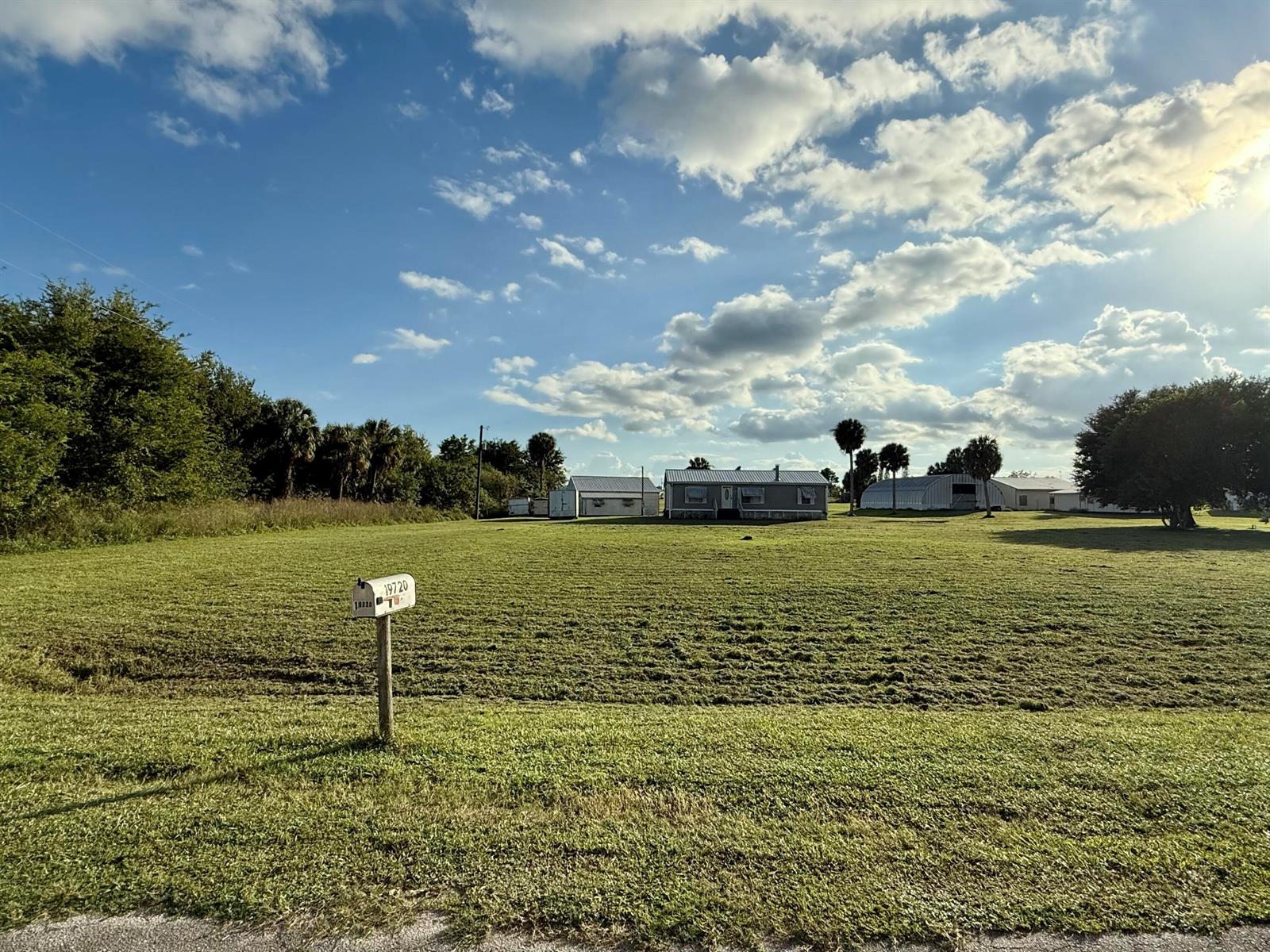A wide, grassy field leads to a single-story house with a mailbox in the foreground — 19720 NW 94th Drive, Okeechobee FL 34972, OKEECHOBEE, FL