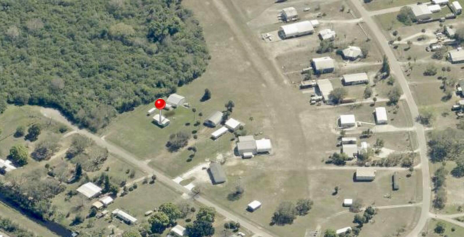 This aerial view shows a residential property with several buildings located near a wooded area — 19720 NW 94th Drive, Okeechobee FL 34972, OKEECHOBEE, FL
