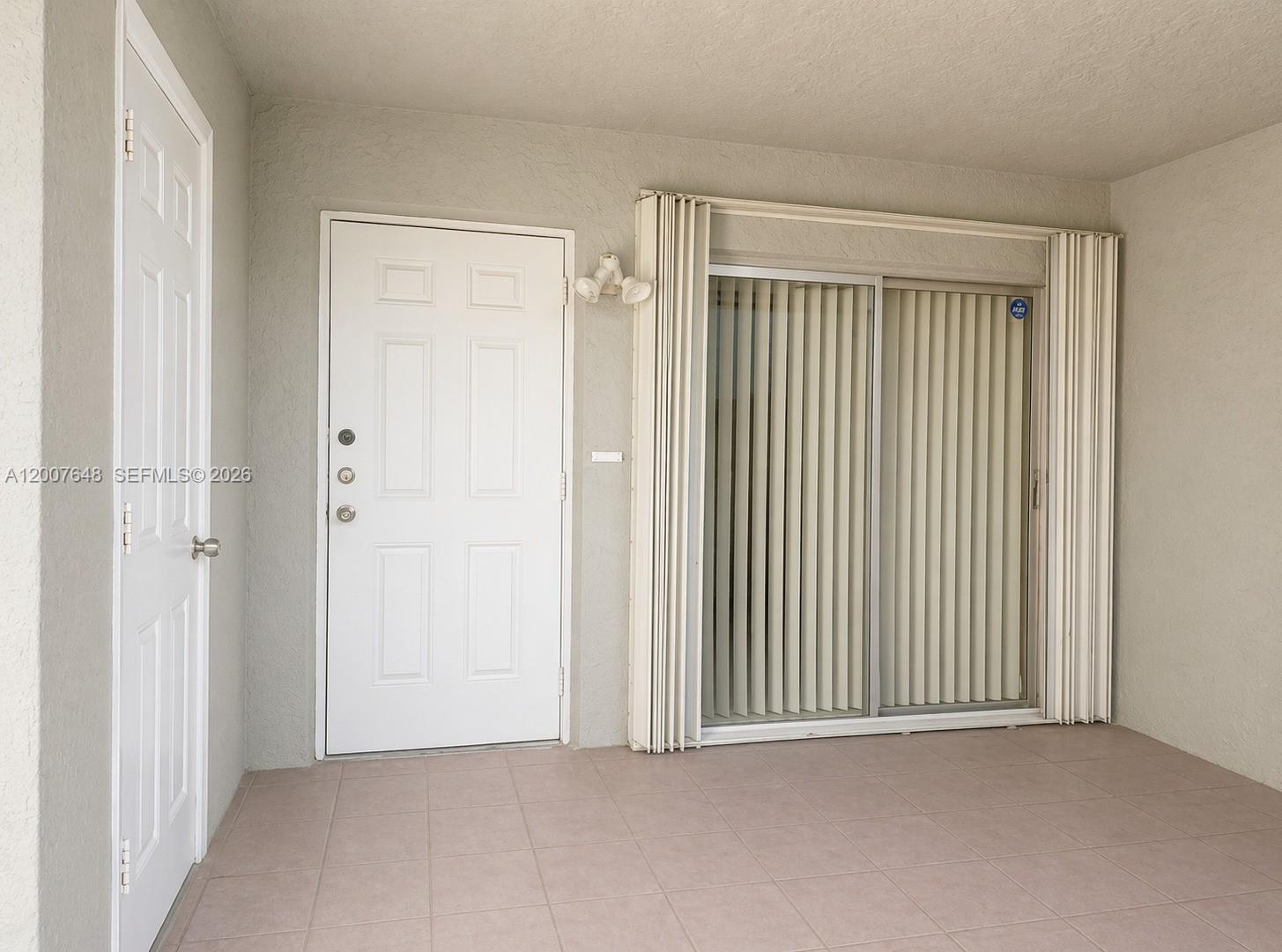 A tiled patio features a white entry door, a sliding glass door, and beige walls — 15400 SW 81st Cir Ln # 1011, Miami FL 33193, MIAMI, FL