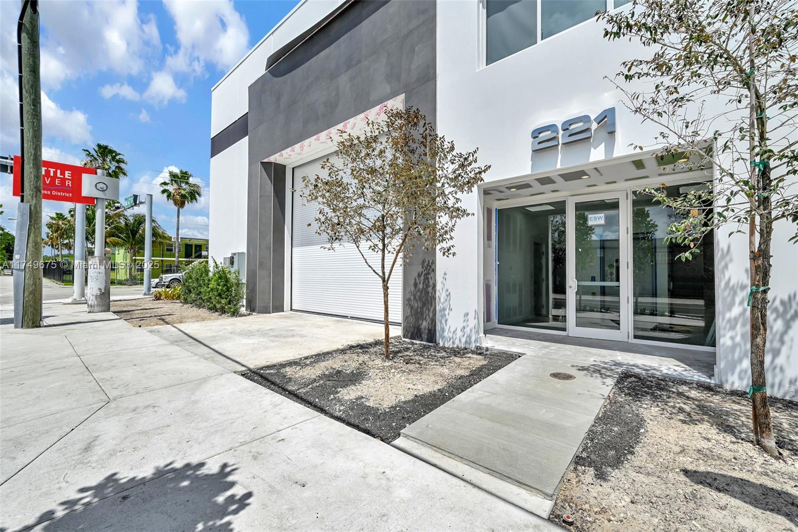 The exterior of a modern commercial building features a roll-up door and glass entrance — 210 NE 68th St # 1, Miami FL 33138, MIAMI, FL